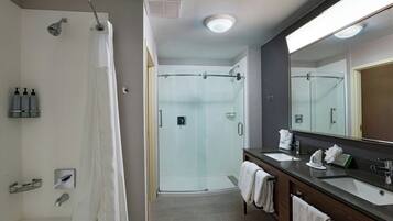 Un baño moderno con ducha envuelta en vidrio, un espejo grande y un lavabo con encimera oscura.