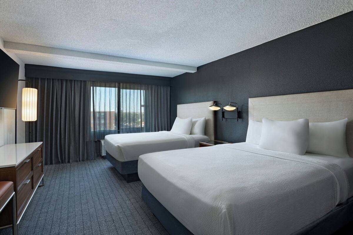 A hotel room with two beds, a desk, and a window with curtains.
