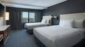 Habitación de hotel con dos camas, un escritorio y una ventana con cortinas.