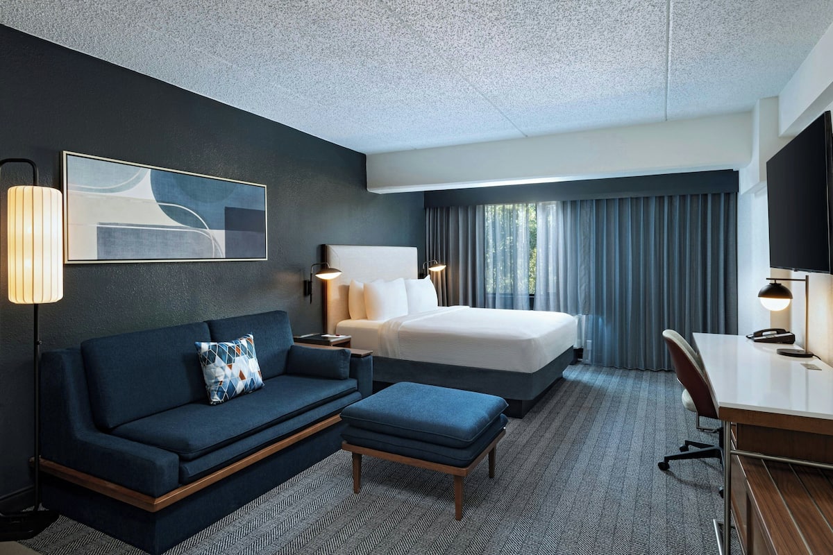 A hotel room with a bed, a sofa, a desk, and a chair.