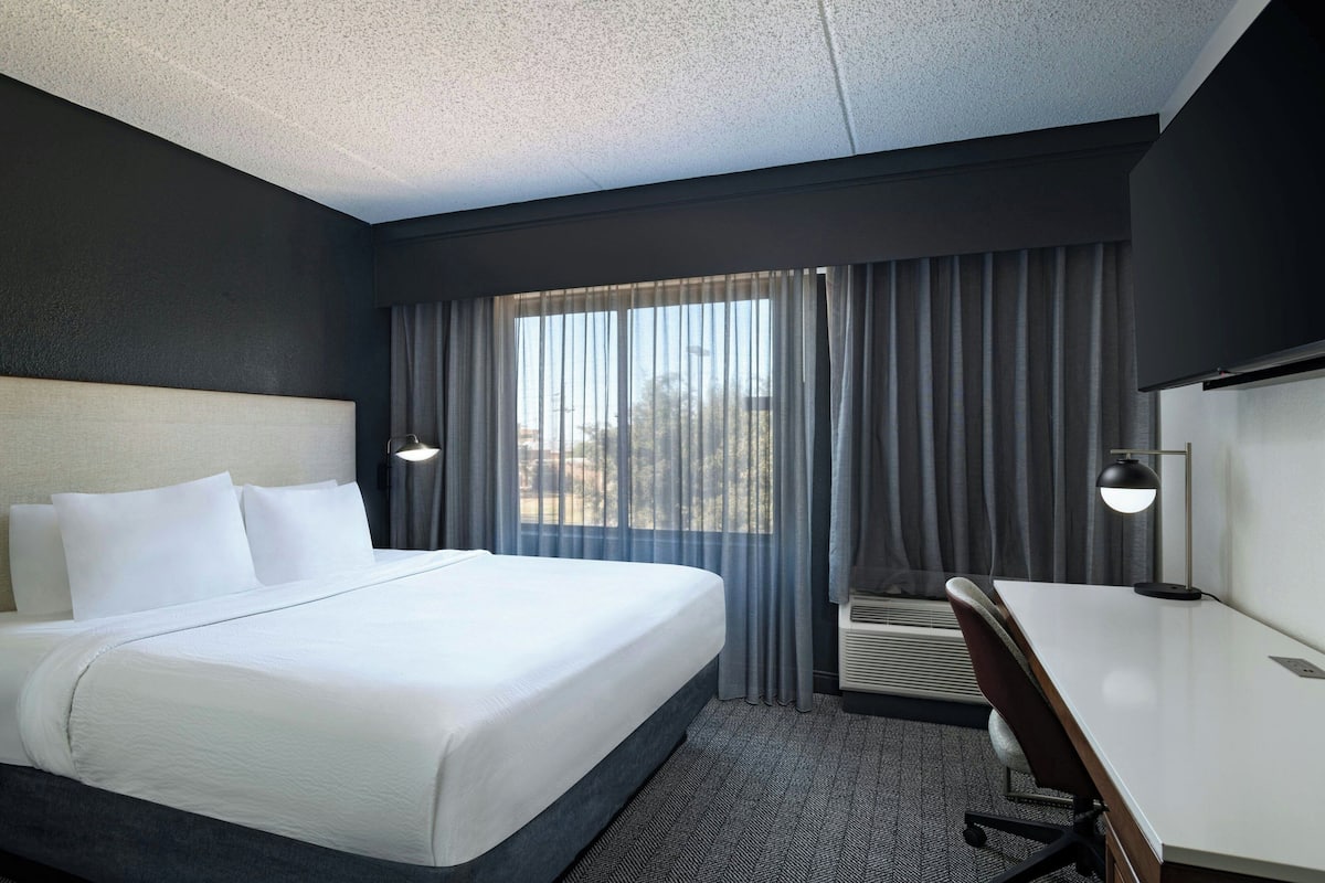 A hotel room with a large bed, a desk, and a window with curtains.