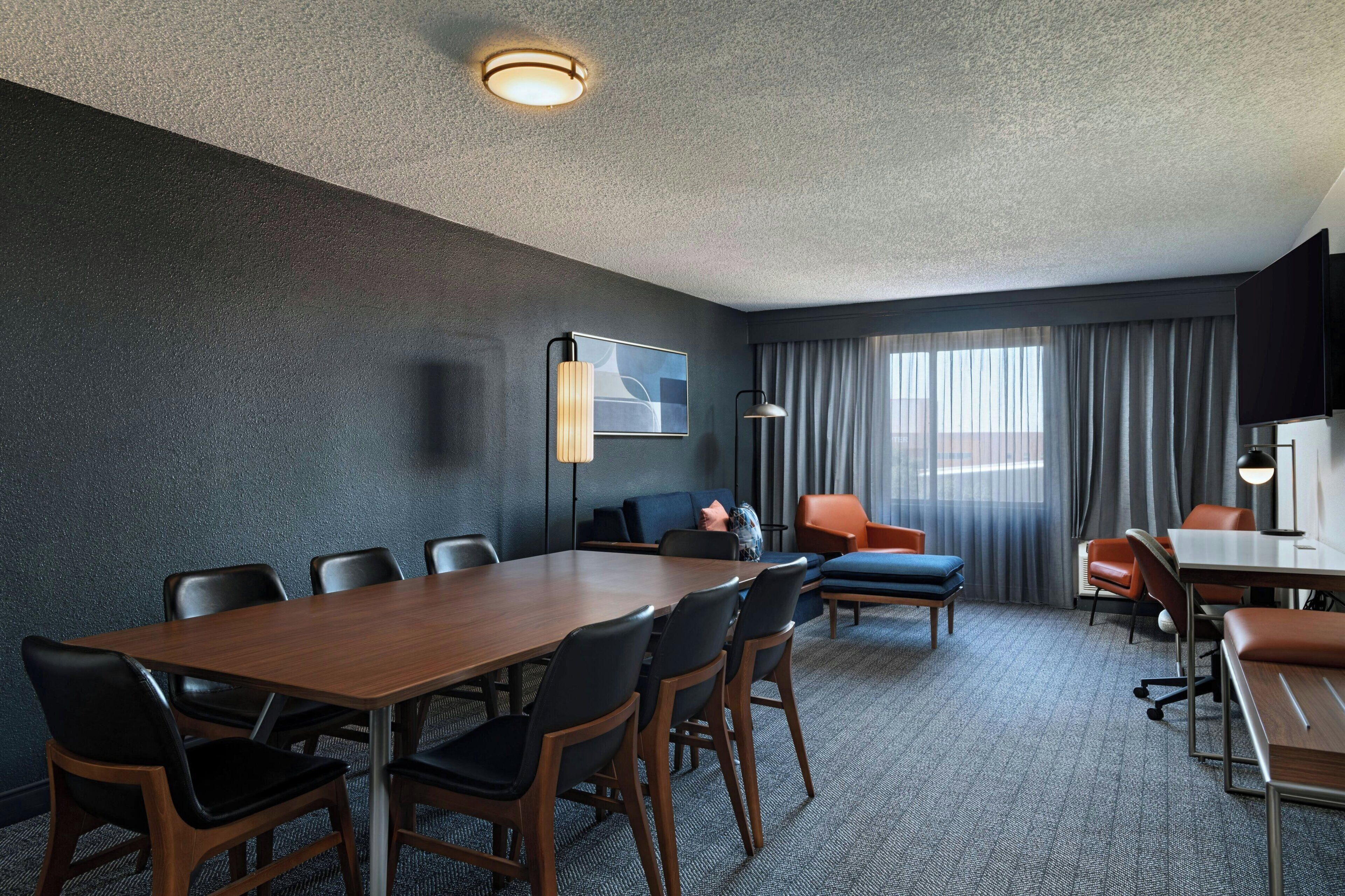 A conference room with a long table, several chairs, a sofa, and a television on the wall.