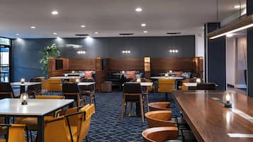 A modern restaurant with wooden tables and chairs, recessed lighting, and a blue patterned carpet.