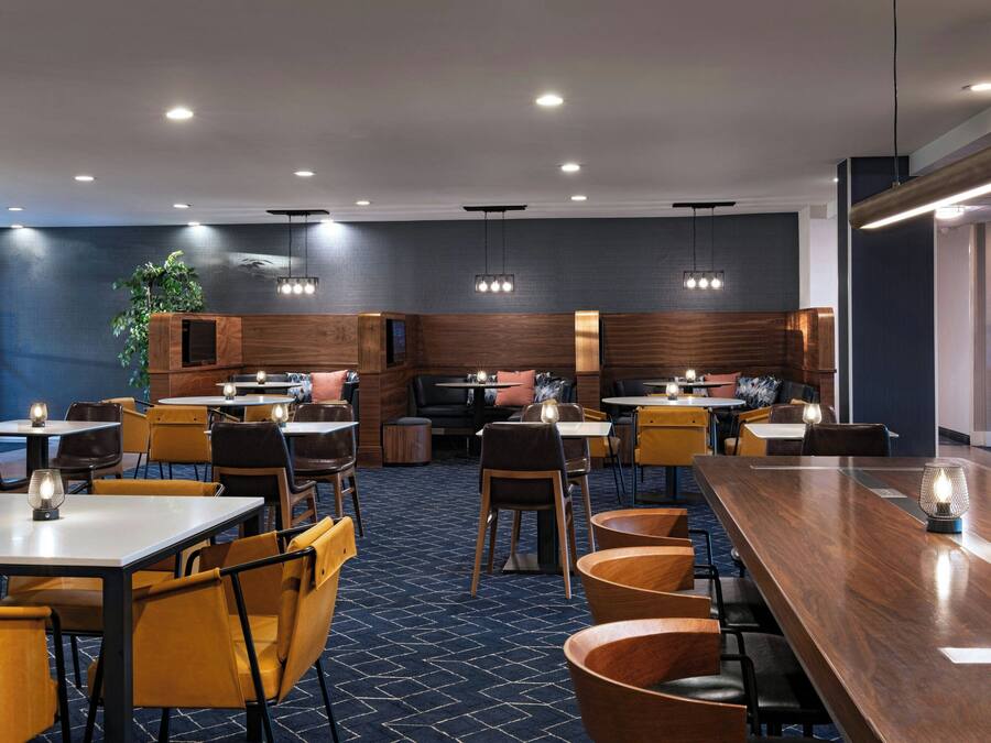 A modern restaurant with wooden tables and chairs, recessed lighting, and a blue patterned carpet.