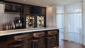 A bar area with a menu board, a coffee machine, and a variety of liquor bottles. There are four stools and a large window with sheer curtains. - Courtyard Marriott Laredo (Laredo)