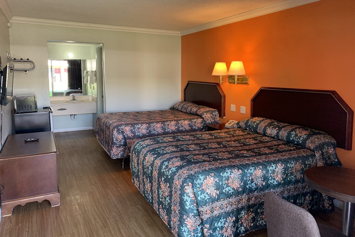 A hotel room with two beds, a desk, a chair, a mirror, and two wall-mounted lamps.