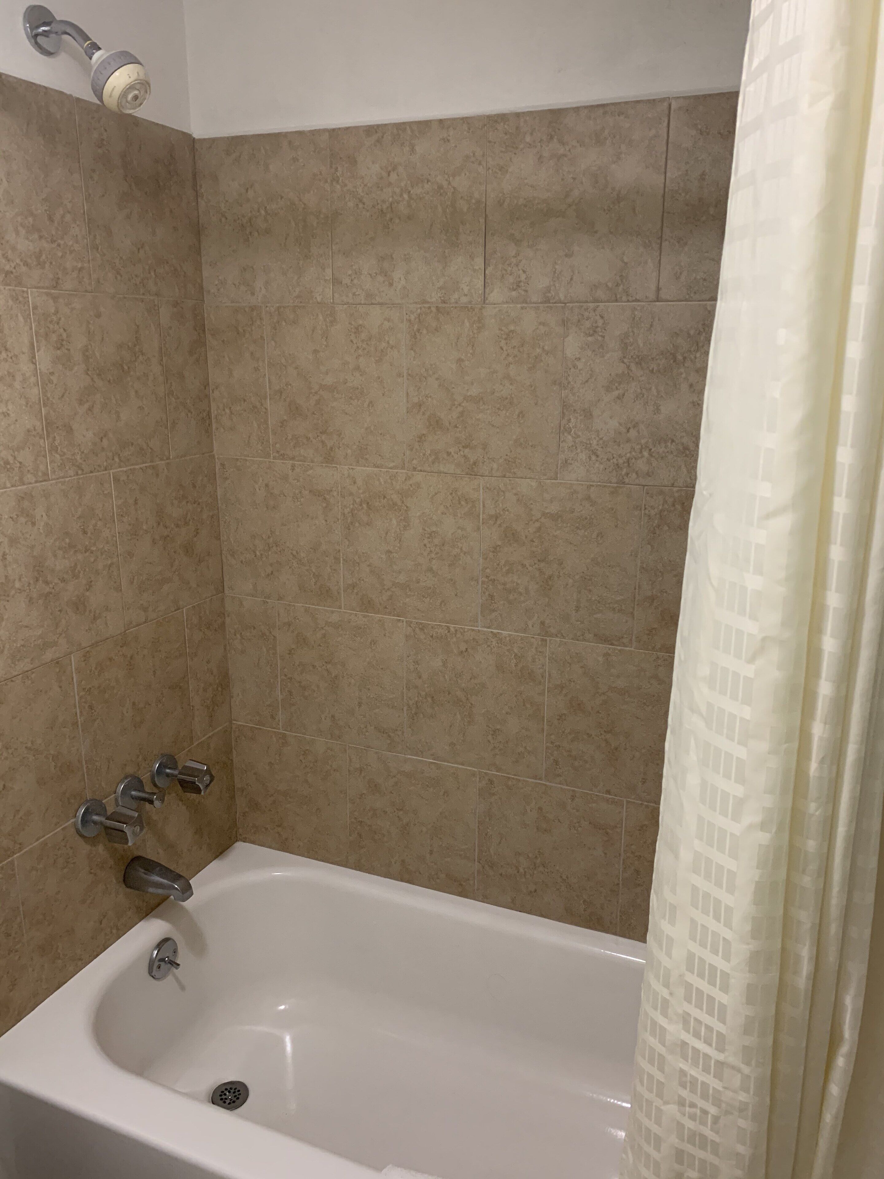 A bathroom with a bathtub, showerhead, and tiled walls.