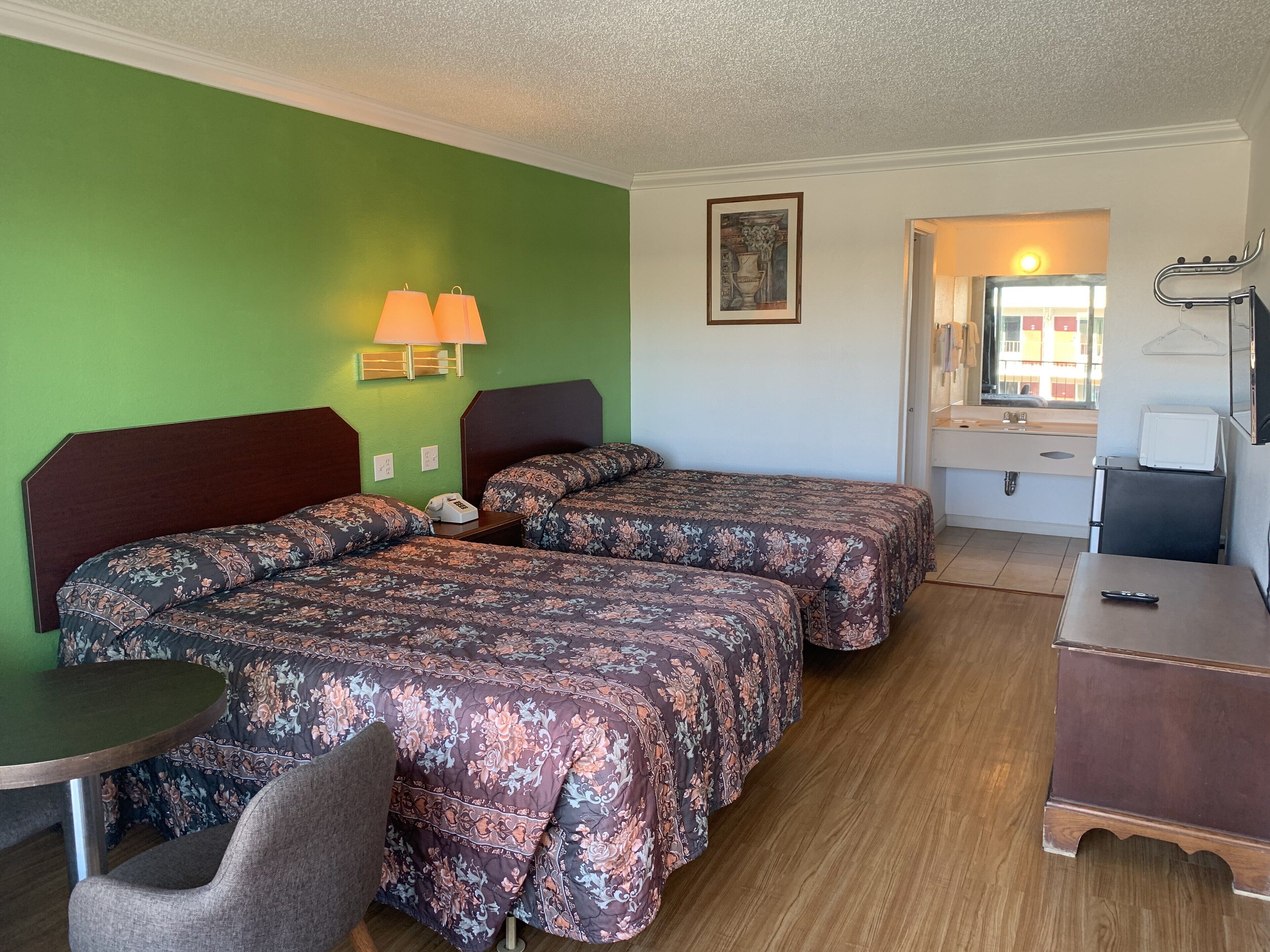 Hotelkamer met twee bedden, een bureau, een stoel, een lamp, een schilderij en uitzicht op het omliggende landschap.