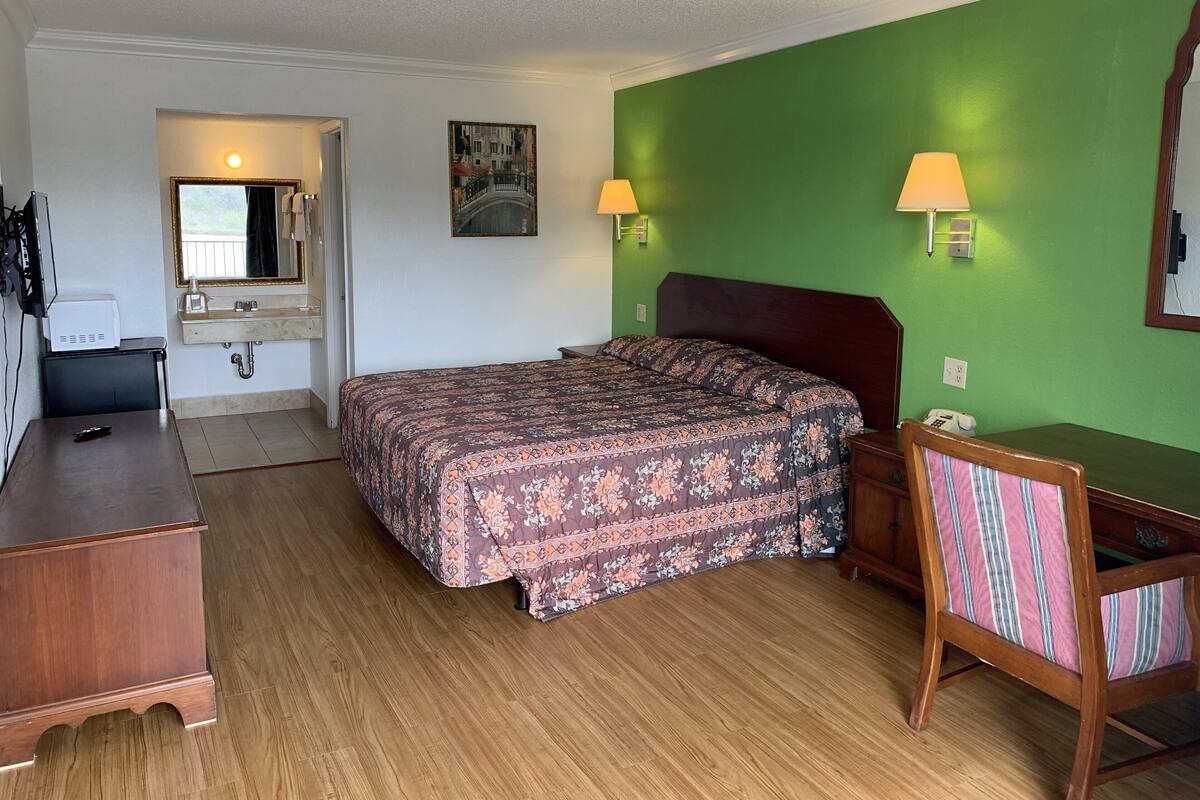 A hotel room with a bed, a desk, a chair, a mirror, a sink, and a window.