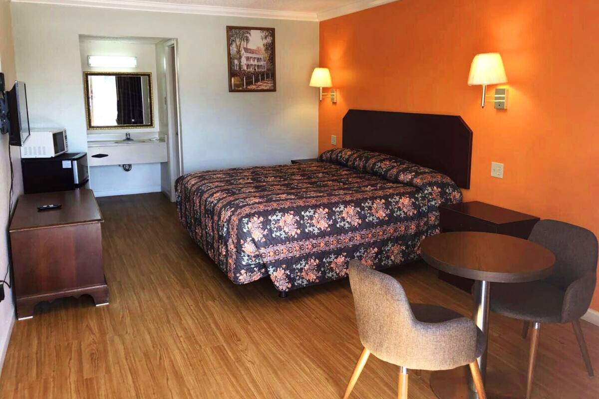 A hotel room with a bed, a desk, a chair, and a small table.