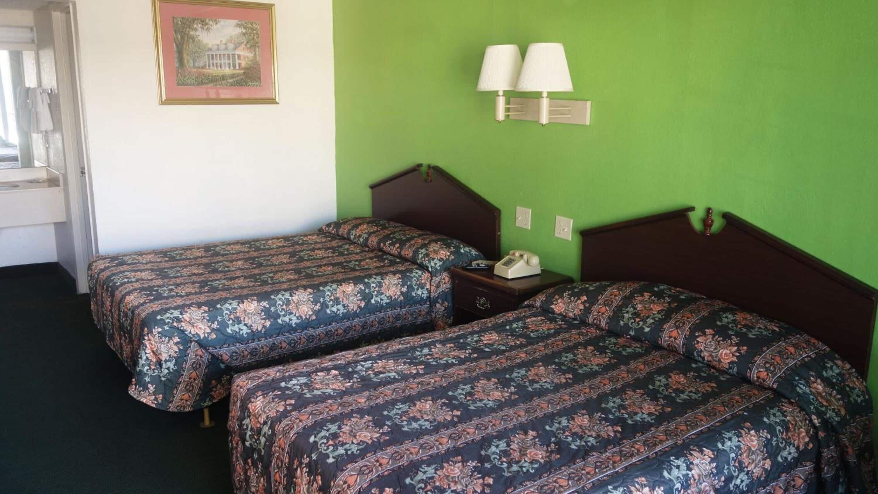 Una habitación con dos camas individuales, una mesita de noche con lámpara y un cuadro enmarcado en la pared.