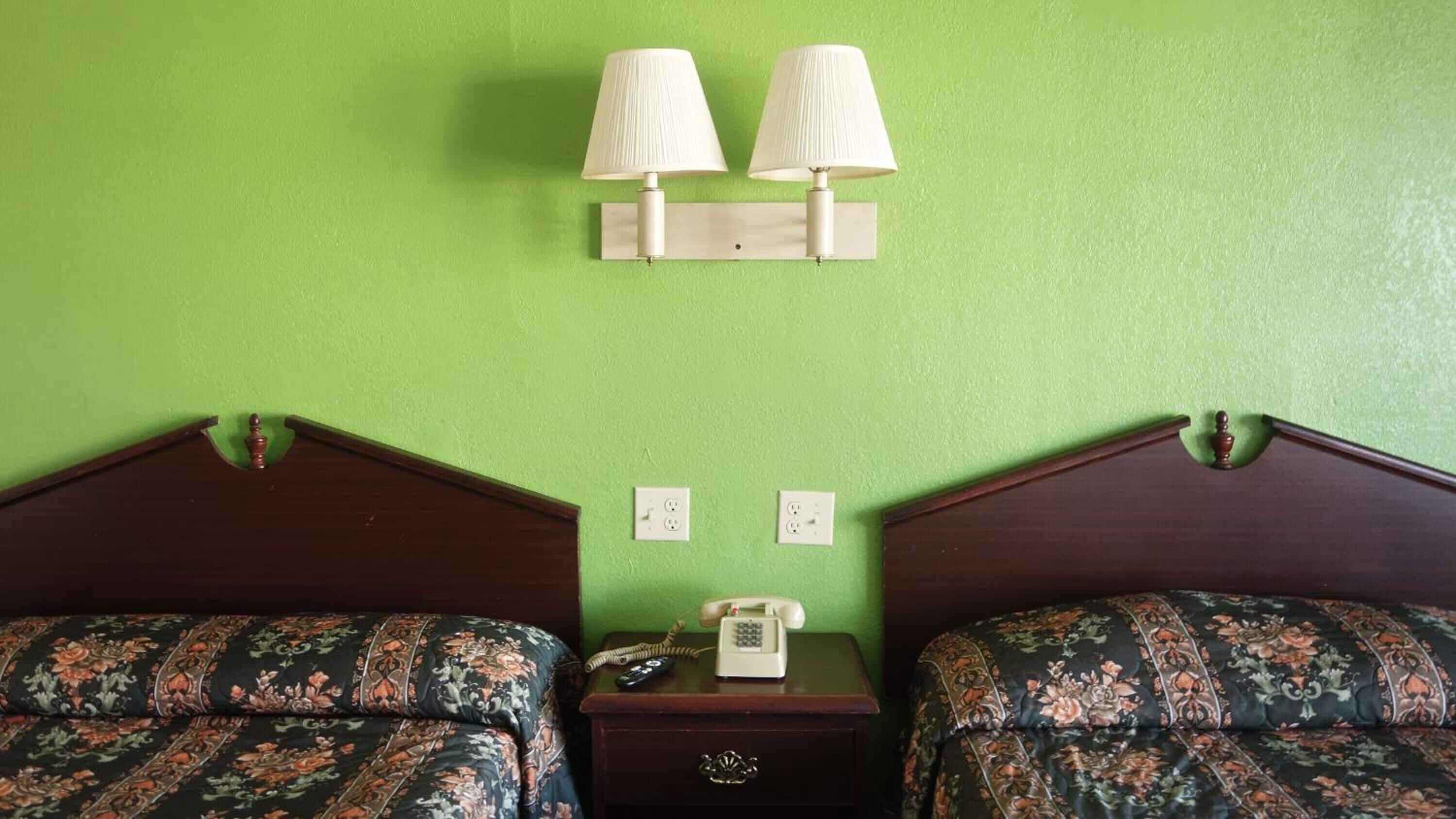 A hotel room with two beds, a nightstand, a telephone, and two wall-mounted lamps.
