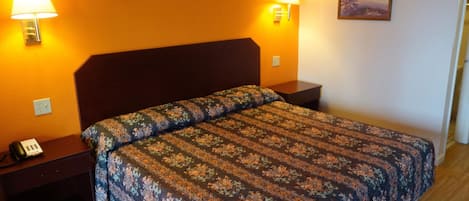 A hotel room with a floral-patterned bedspread, two bedside lamps, a nightstand with a telephone, and a painting on the wall.