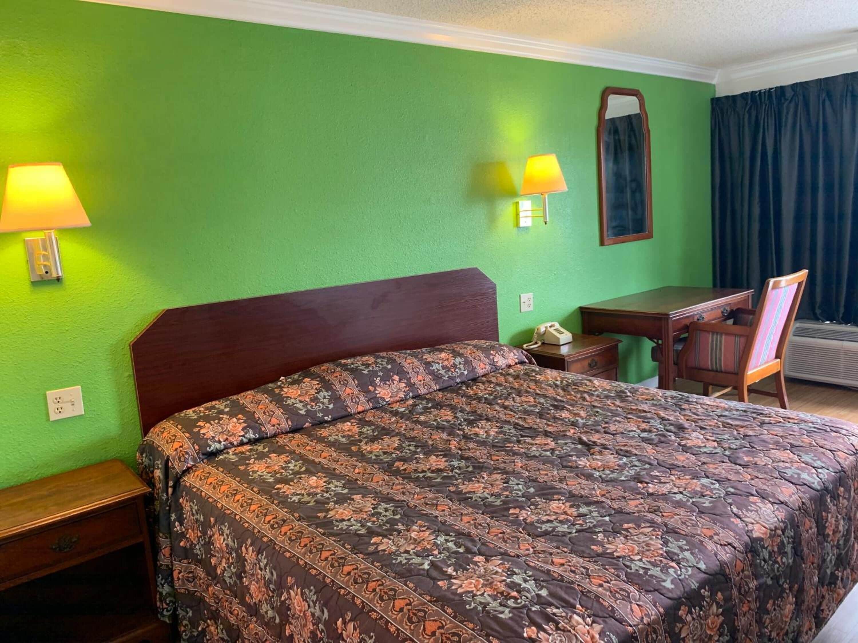 Habitación de hotel con cama, escritorio, silla y espejo.