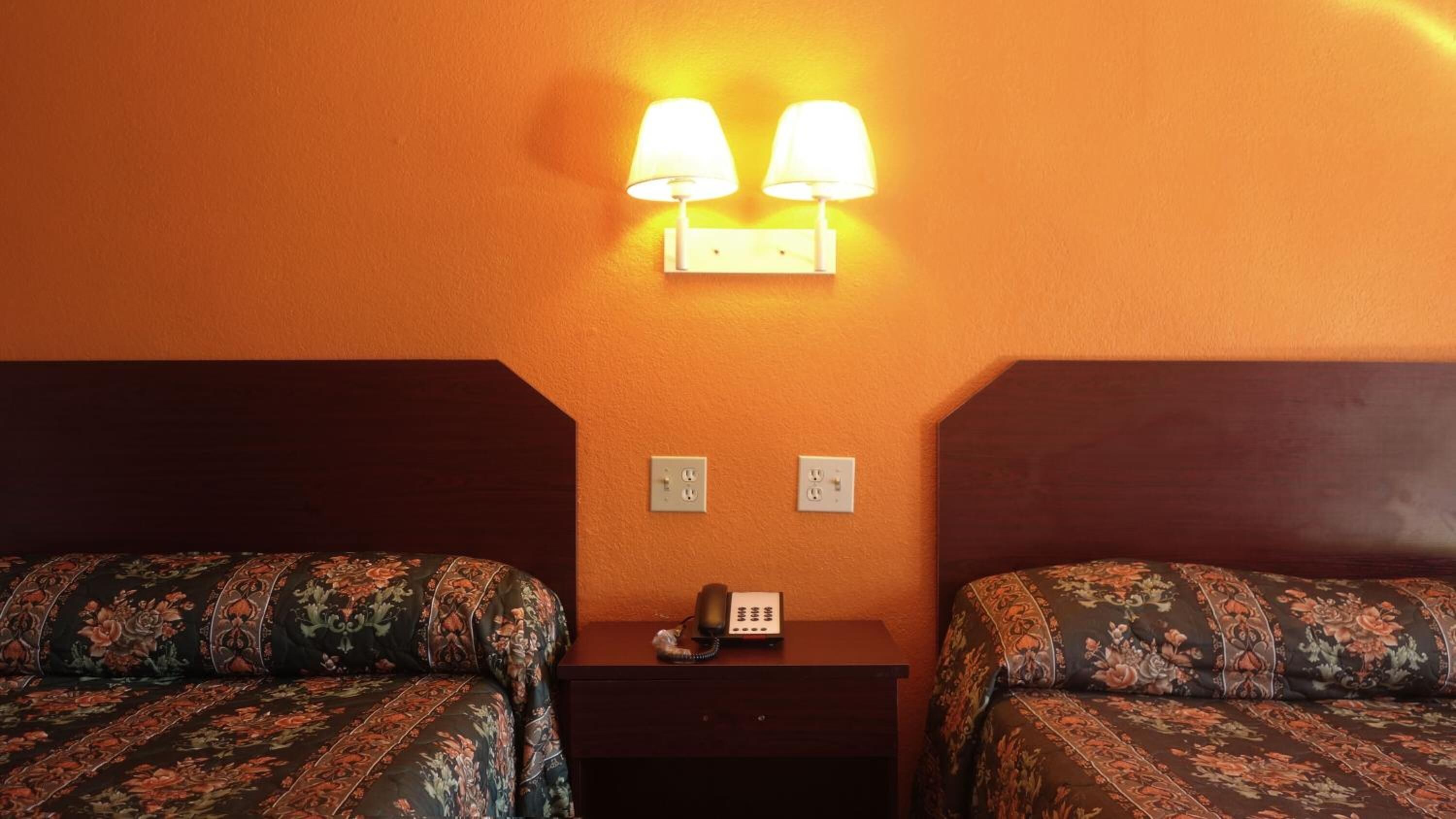 Een hotelkamer met twee bedden, een nachtkastje en een telefoon aan de muur.