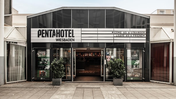 A modern pentahotel with a glass facade, a clear entrance, and two potted plants at the entrance. - pentahotel Wiesbaden (Wiesbaden)