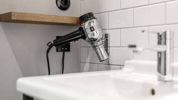 A bathroom with a white sink, a wooden shelf, and a handheld hair dryer mounted on the wall.