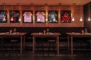 A restaurant with a brick wall, framed jerseys, and hanging light fixtures.