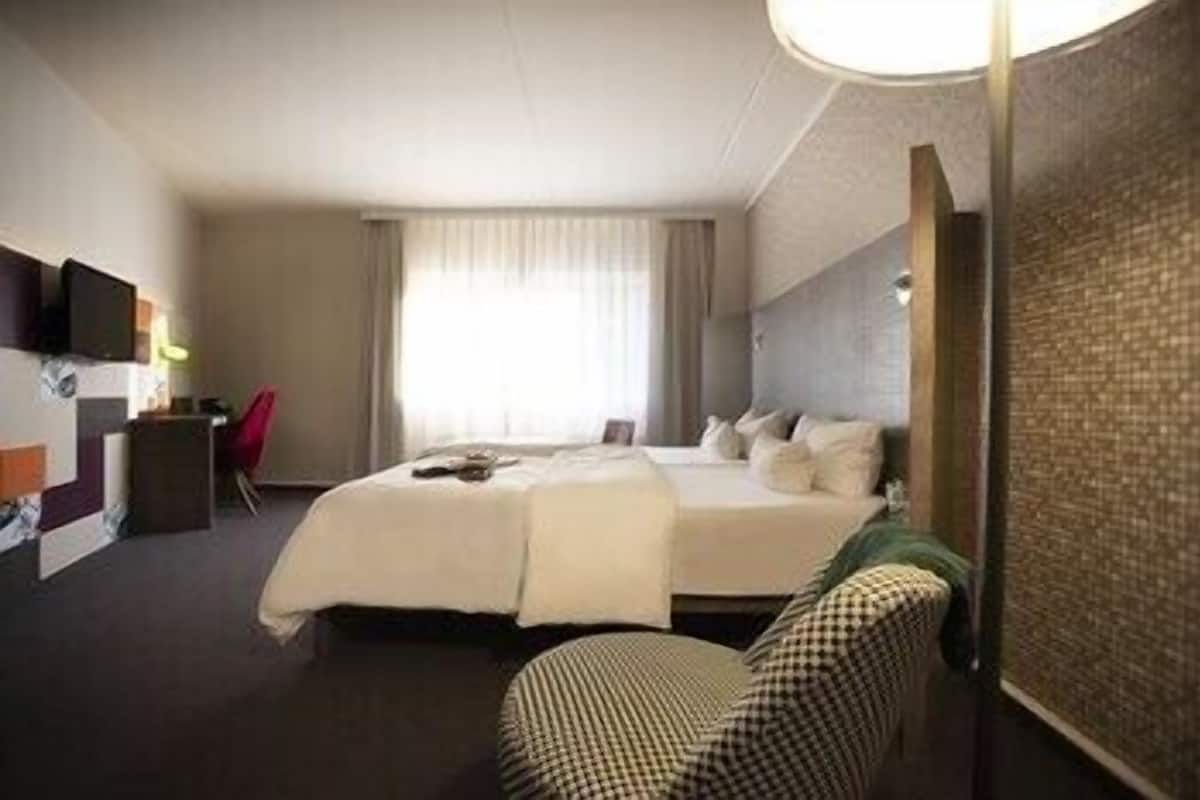 Quarto de hotel com cama, escrivaninha, cadeira e televisão.