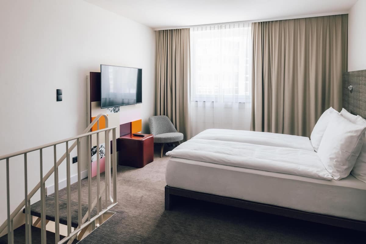 Quarto de hotel com uma cama, televisão, cadeira e escada.