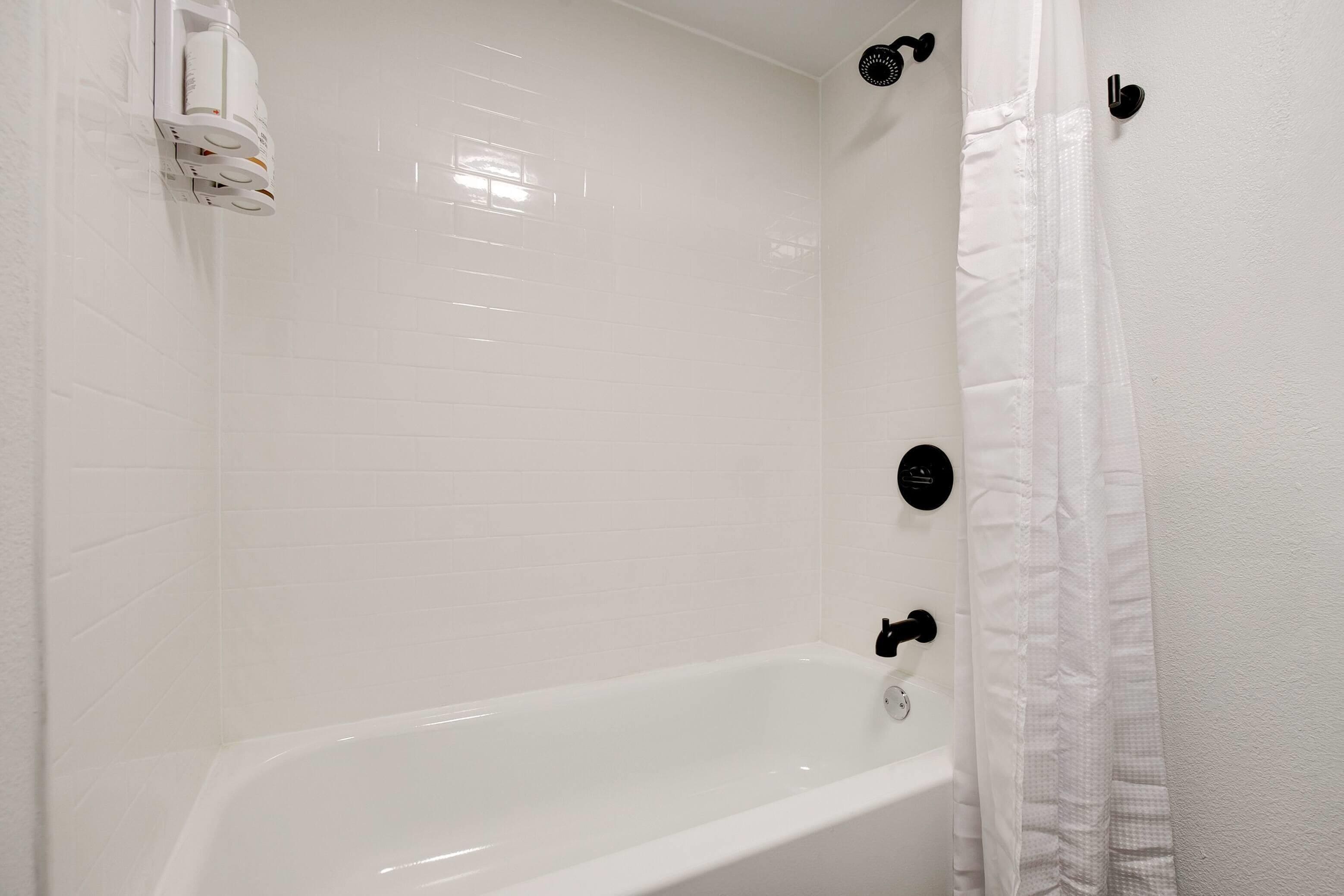A white bathtub in a bathroom with white tiled walls and a white shower curtain.