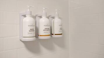 Three white toiletry bottles with pump dispensers mounted on a white tiled wall.