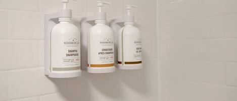 Three white toiletry bottles with pump dispensers mounted on a white tiled wall.