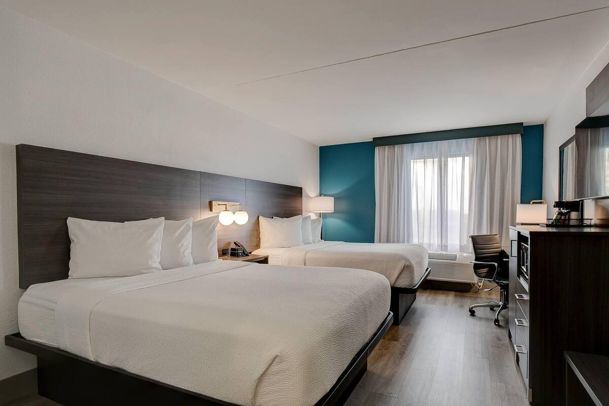 Habitación de hotel con dos camas, un escritorio, una silla y un televisor.
