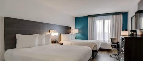 Habitació d'hotel amb dos llits, una taula de treball, una cadira i un televisor.