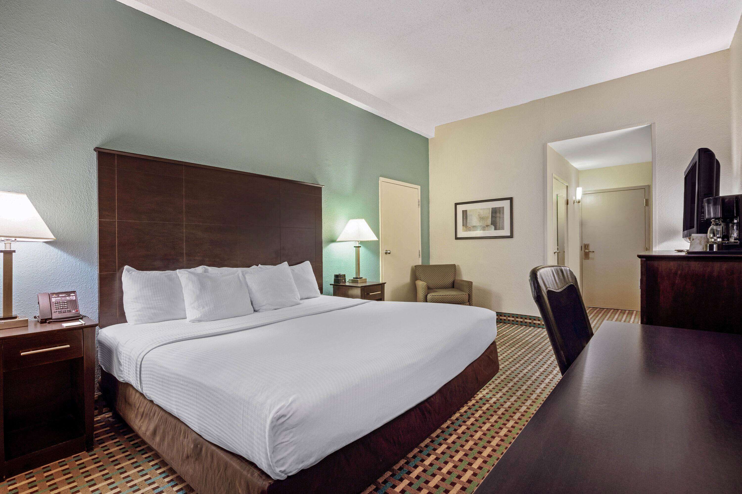 A hotel room with a large bed, a desk, a chair, a lamp, and a television.