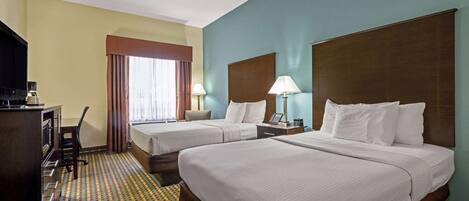 A hotel room with two beds, a desk with a lamp, a television, and a patterned carpet.