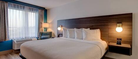 A hotel room with a large bed, bedside lamps, a nightstand, and a wall-mounted clock.