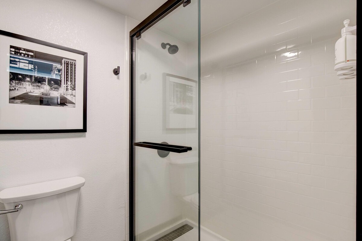A bathroom with a glass shower enclosure, a white toilet, and a framed photograph on the wall.