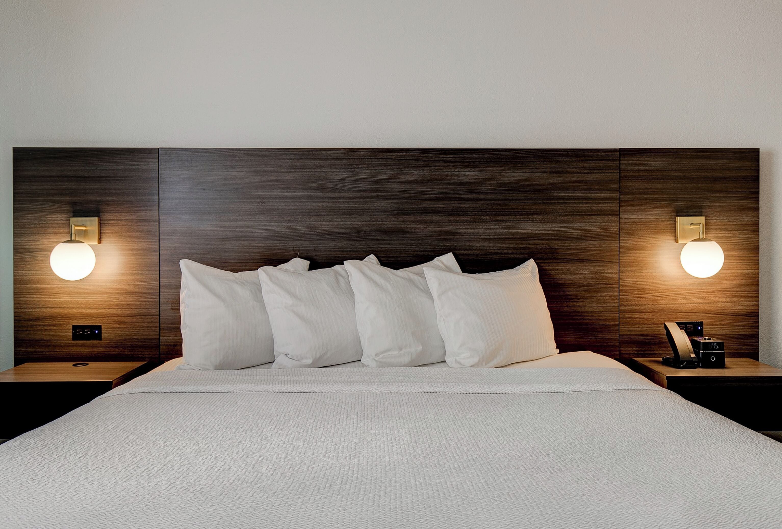 Une chambre d’hôtel avec un grand lit, deux tables de chevet et des lampes fixées au mur.