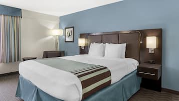 A hotel room with a large bed, two bedside tables, a nightstand, a lamp, and a framed picture on the wall.