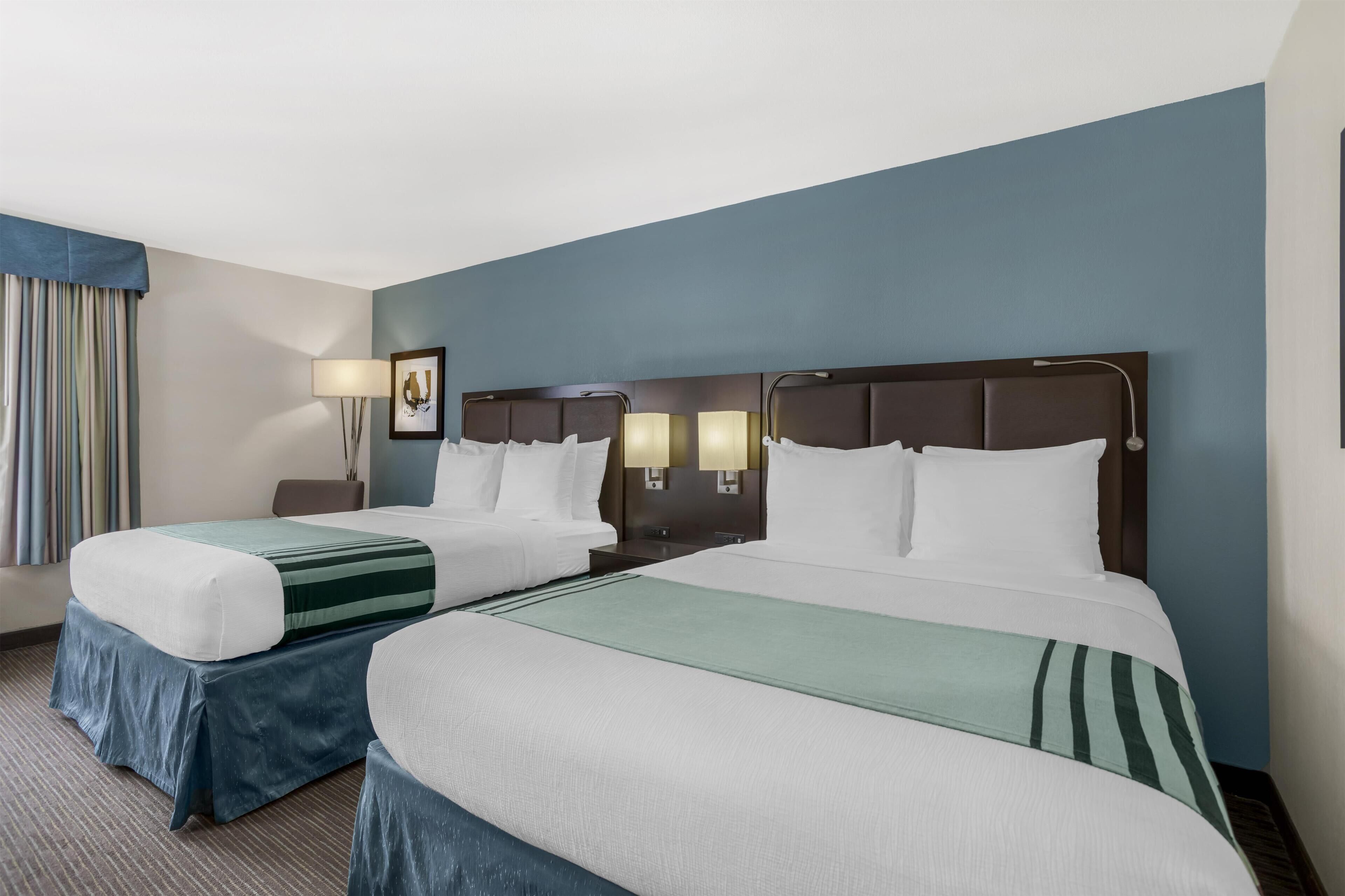 A hotel room with two beds, a nightstand, a lamp, and a picture on the wall.