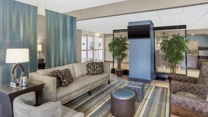 Een moderne hotellobby met een bank, fauteuils, een salontafel en twee potplanten.