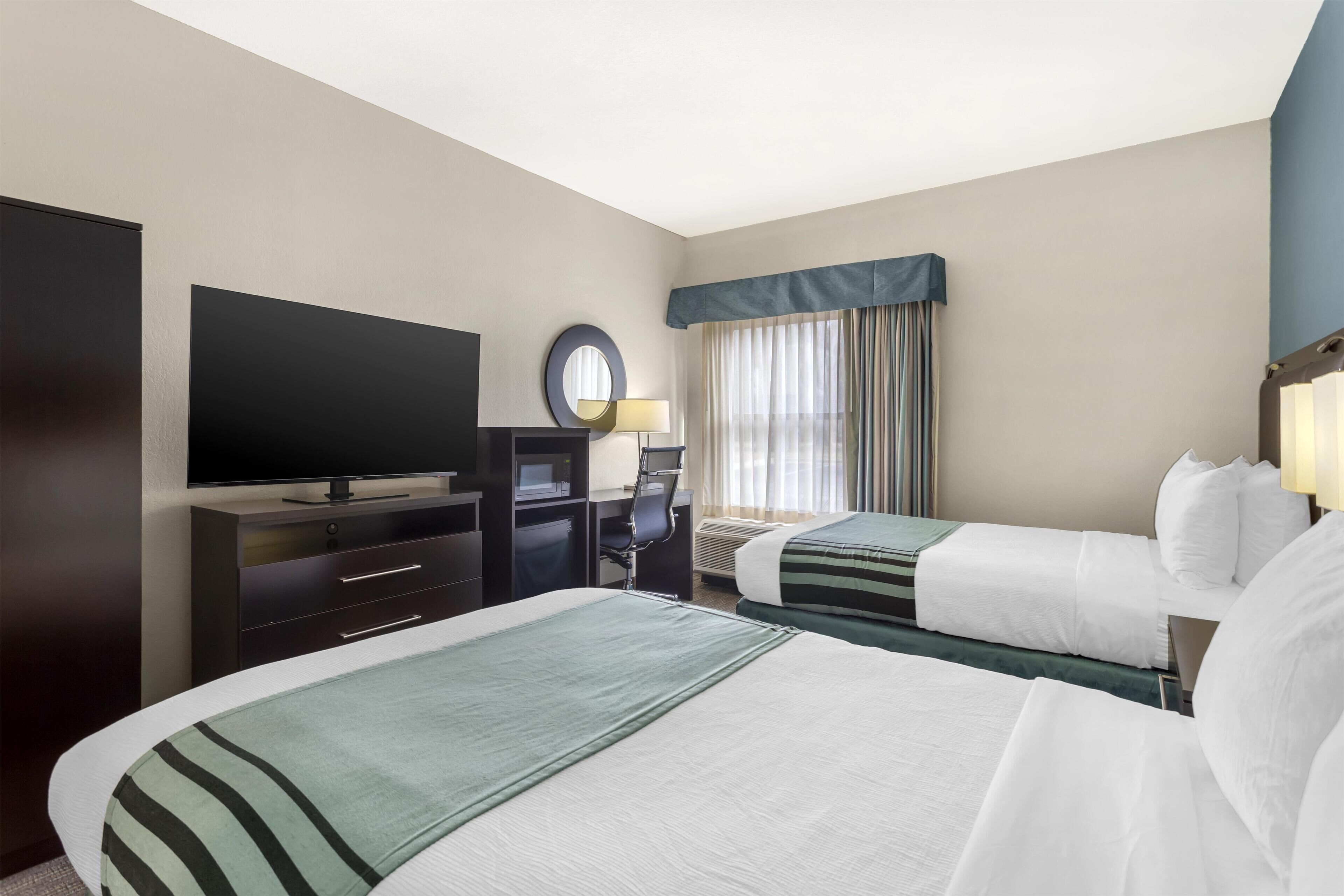 Quarto de hotel com duas camas, uma escrivaninha, uma televisão e uma janela com cortinas.