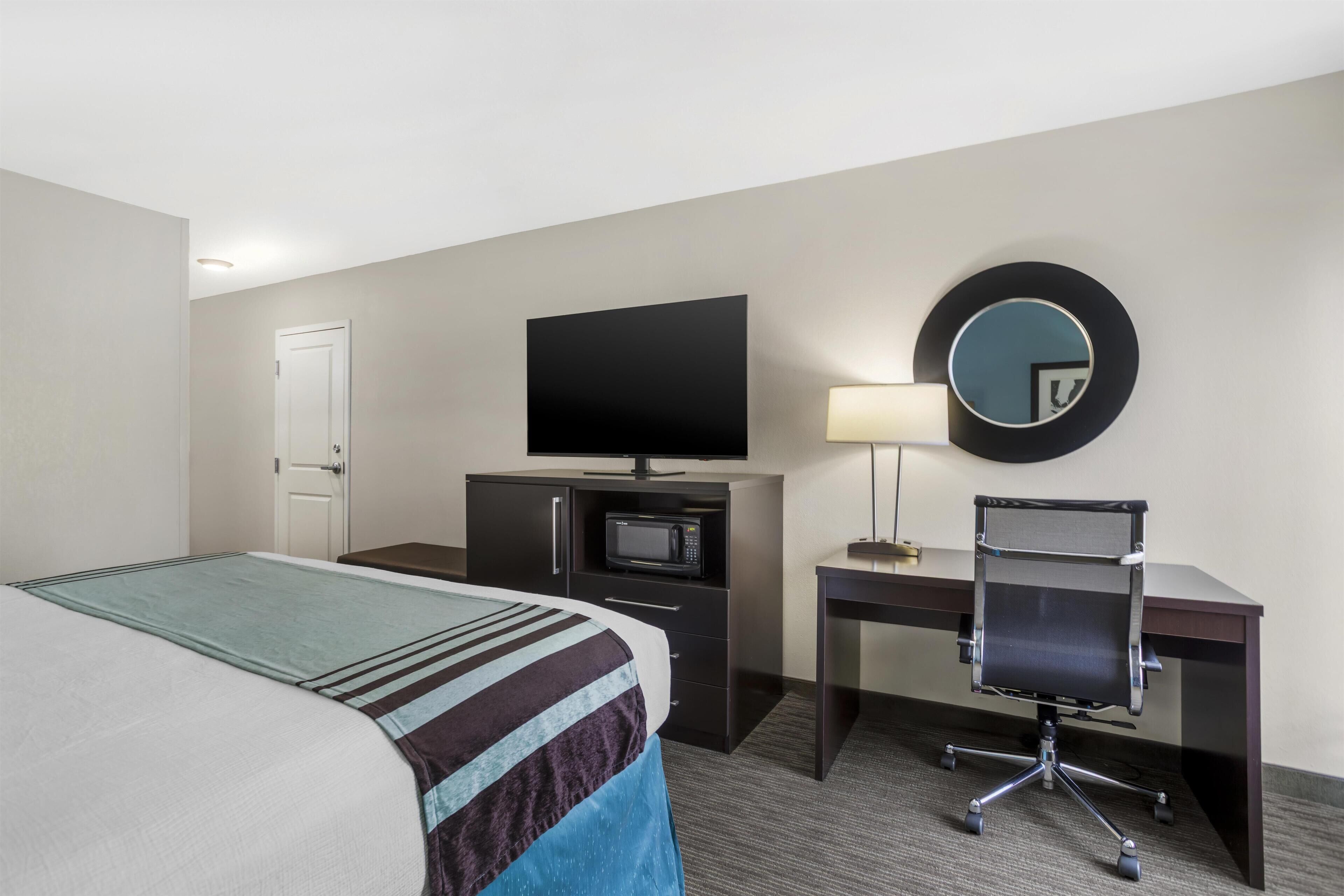 A hotel room with a bed, a desk with a chair, a television, a microwave, and a mirror.