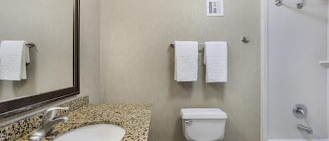 A bathroom with a granite countertop sink, a toilet, a bathtub, and a mirror.