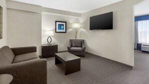 Een hotelkamer met een bank, een salontafel, een stoel, een televisie, een lamp en een schilderij aan de muur.