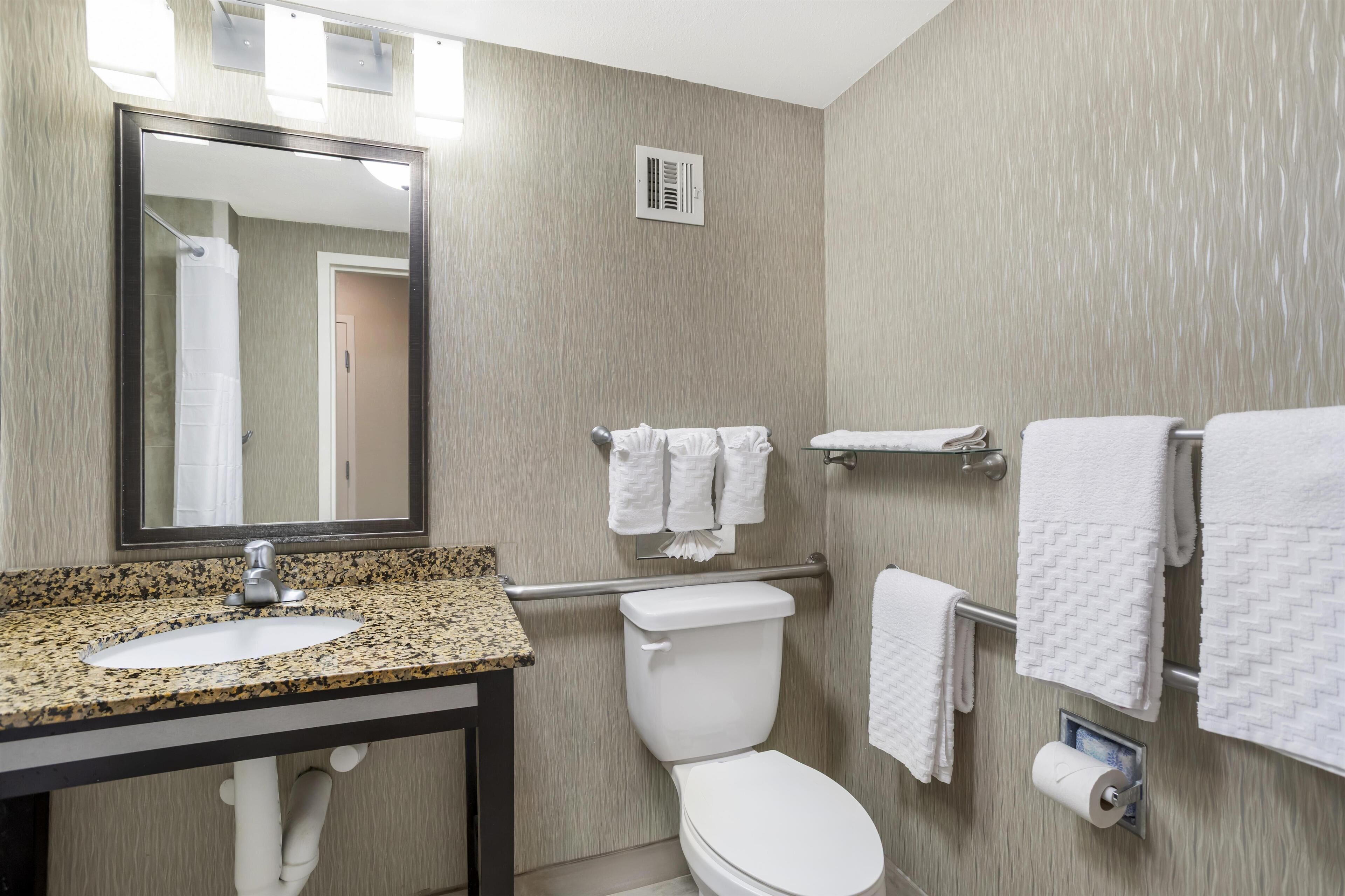A bathroom with a granite countertop sink, a white toilet, a towel rack, and a mirror.