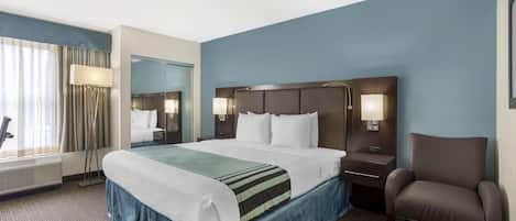 A hotel room with a large bed, a chair, a desk, and a mirror.