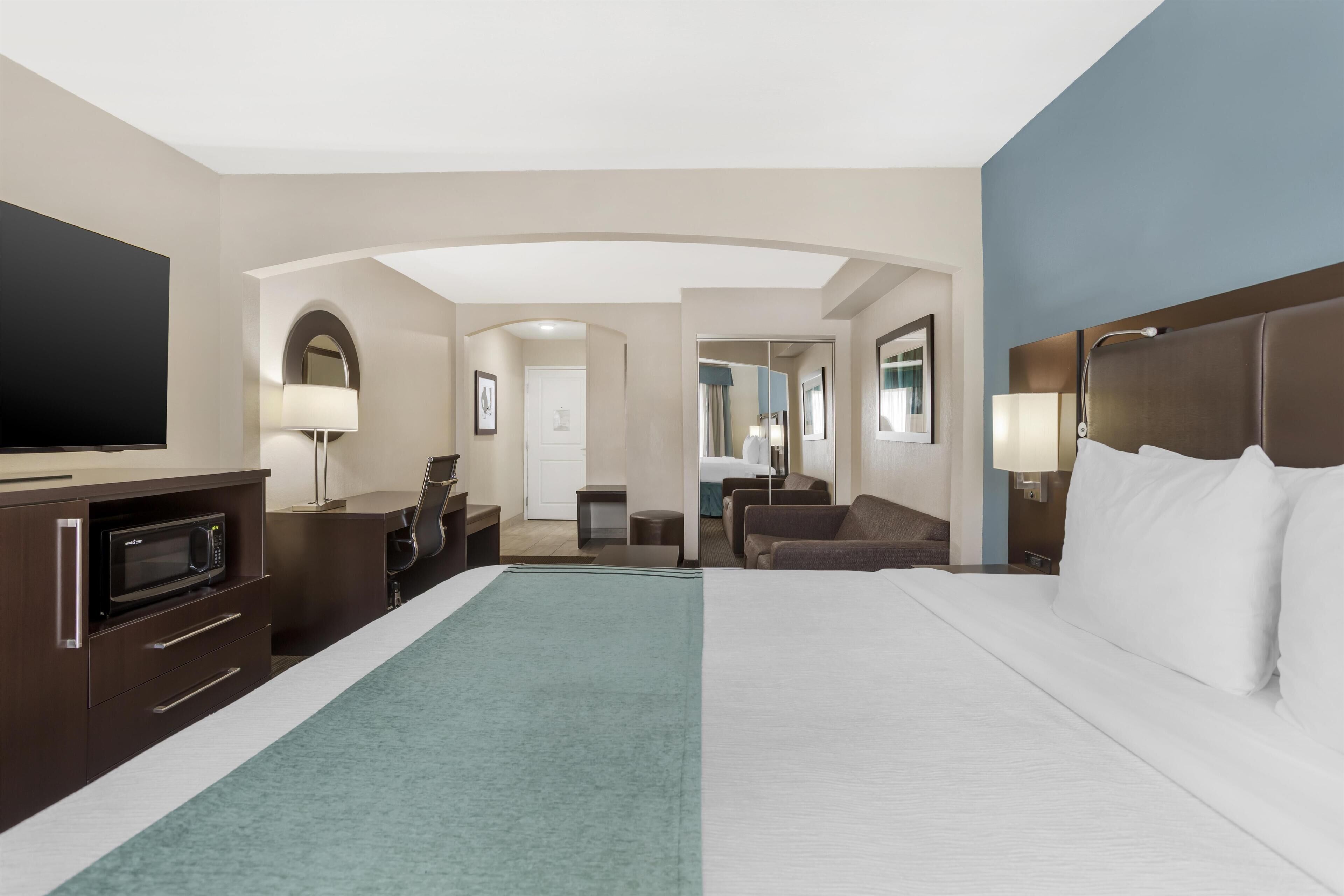 Une chambre d’hôtel comprenant un lit, un bureau avec un micro-ondes, une télévision, un canapé et une salle de bain visible à travers une arche.