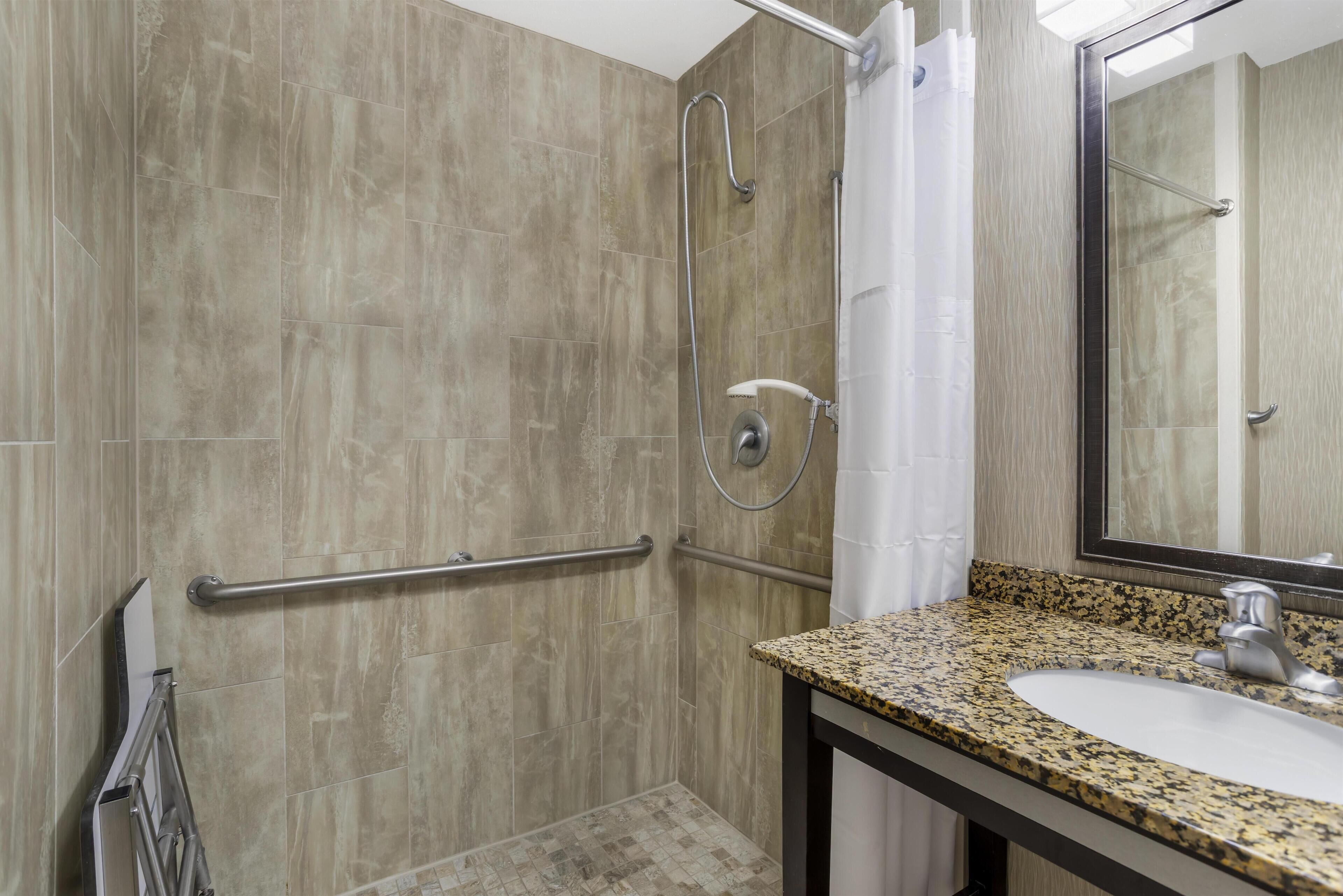 Ein Badezimmer mit Dusche, Haltegriffen, Waschbecken und Spiegel.