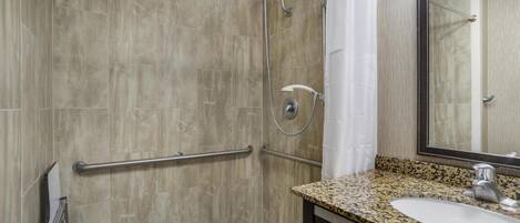 A bathroom with a shower, grab bars, a sink, and a mirror.