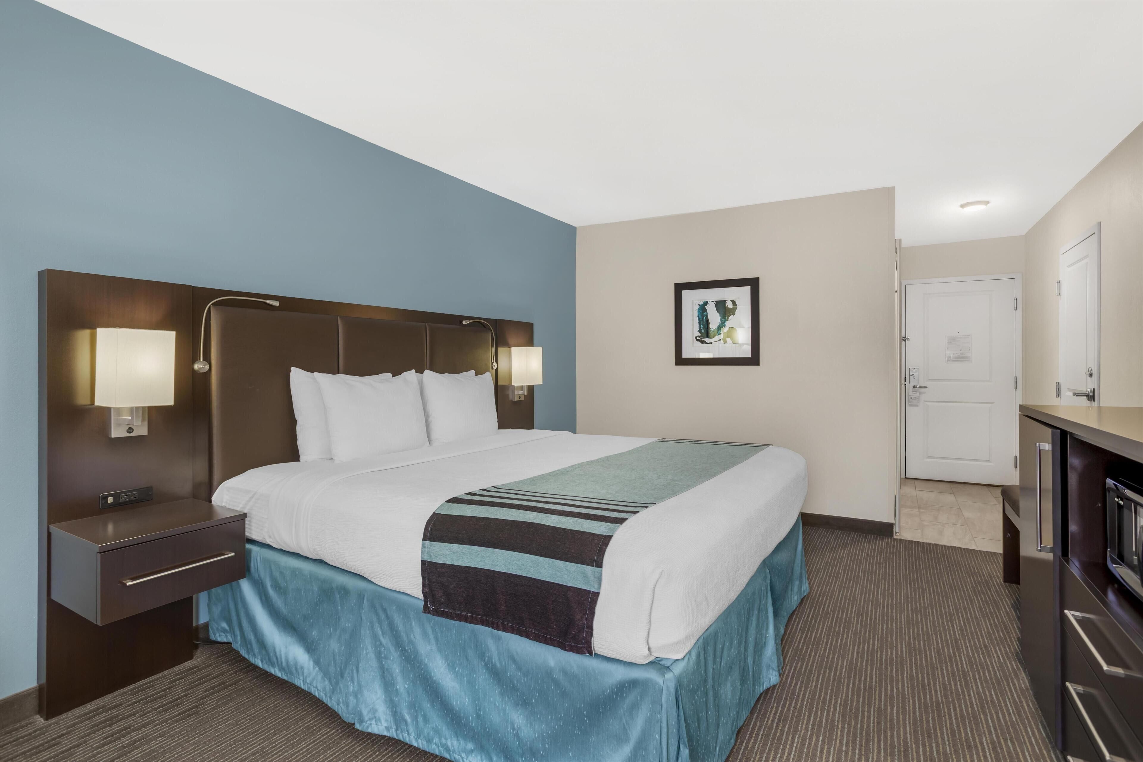 A hotel room with a large bed, bedside lamps, a nightstand, a framed picture on the wall, and a door to the right.