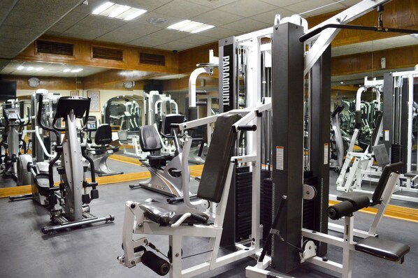 A gym with various exercise machines, mirrors, and a wooden wall.