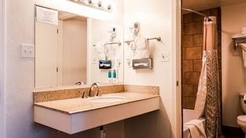 A bathroom with a sink, mirror, hair dryer, and shower curtain.