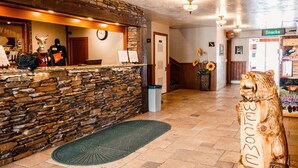 A reception area with a stone wall, a wooden reception desk, a clock, and a wooden bear sculpture. - White Buffalo (West Yellowstone)